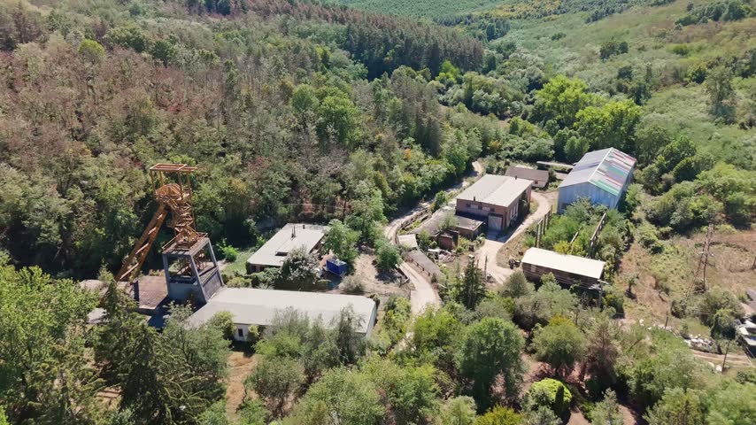 Aerial view of the historic Tiribesi-Akna coal mine headframe and industrial buildings amid summer forest in Bátonyterenye, Hungary, in the Mátra region.