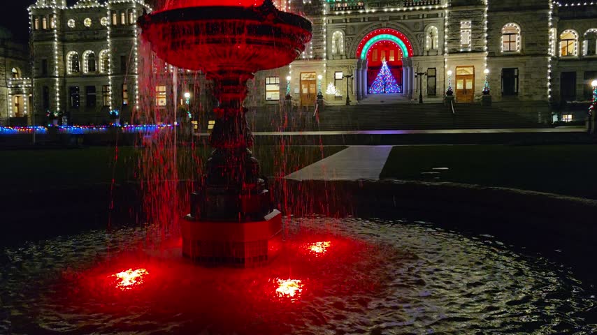 Historic British Columbia provincial parliament building at night illuminated with Christmas lights, Victoria, BC, Canada. Slow pan up motion with fountain.