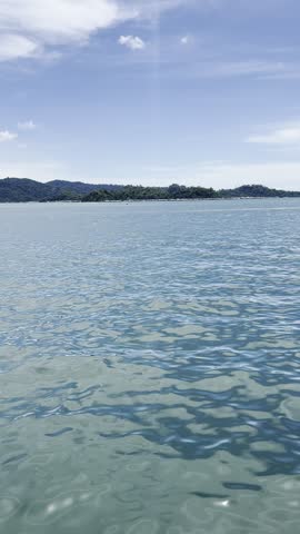 Beautiful Blue Sea with Gentle Waves, Green Coastal Landscape and Blue Sky with White Clouds