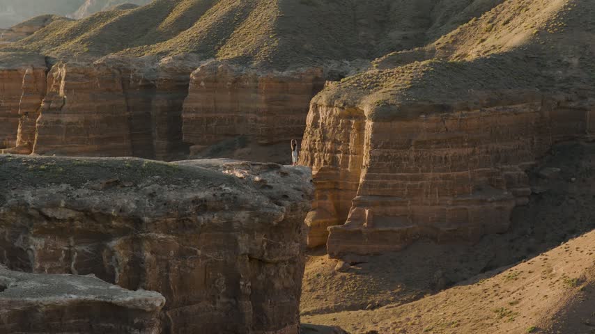 Aerial view of a person standing on the edge of a cliff in Charyn Canyon National Park with rocky formations and golden hour light in Tamerlik, Almaty Region, Kazakhstan.