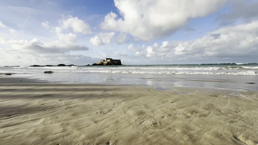 Scenic view of Fort National on the beach of Sillon in Saint-Malo with gentle waves washing on wet sand under a cloudy sky in Brittany, France
