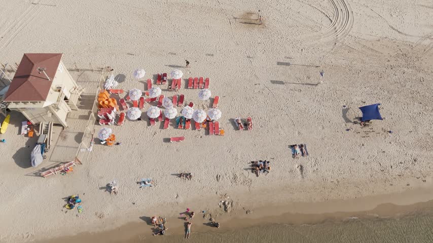 Aerial view of Nemal Tel Aviv beach with a lifeguard tower, sun umbrellas, and people relaxing on the sand in Tel Aviv-Yafo, Tel Aviv District, Israel.