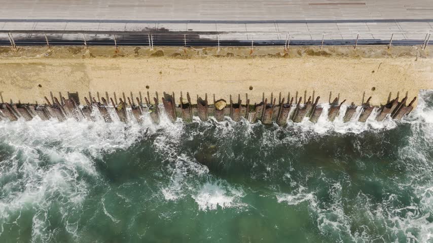 Aerial view of the sea wall and metal pilings at the Port of Tel Aviv with waves crashing against the structure in Tel Aviv-Yafo, Tel Aviv District, Israel.
