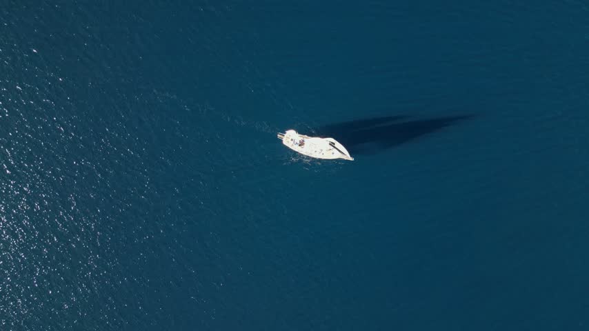Aerial view of a small white boat sailing on deep blue sea, casting a long shadow in Moraira, Valencian Community, Spain.