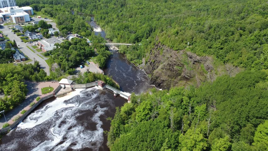 Drone footage captures a tourist walkway above a waterfall cascading to the base of a cliff near an old hydroelectric power plant in Rivière-du-Loup, Quebec.