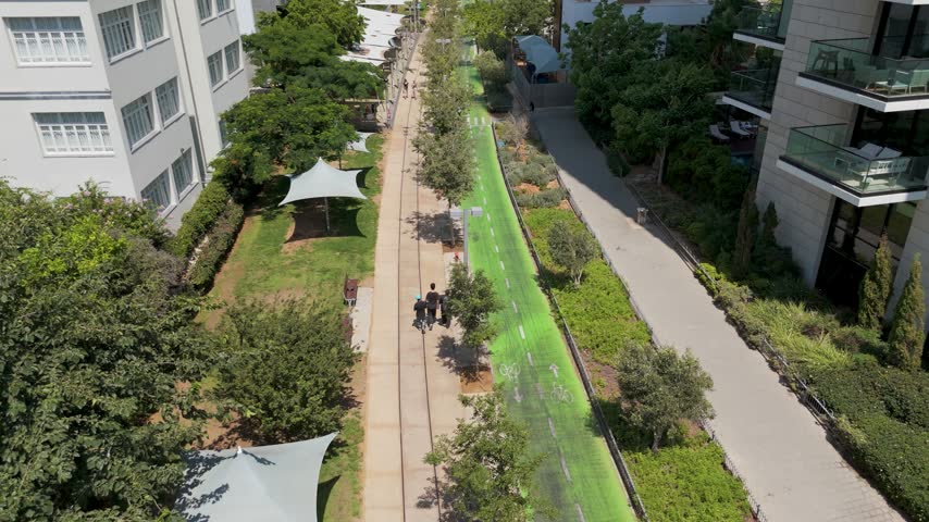 Aerial view of HaMesila Park featuring a green bike path, walking trails, and lush trees alongside modern residential buildings in Tel Aviv-Yafo, Tel Aviv District, Israel.