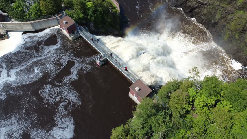 Tourists gaze at a roaring waterfall from a pedestrian walkway positioned at the summit in Rivière-du-Loup, Quebec, Canada.