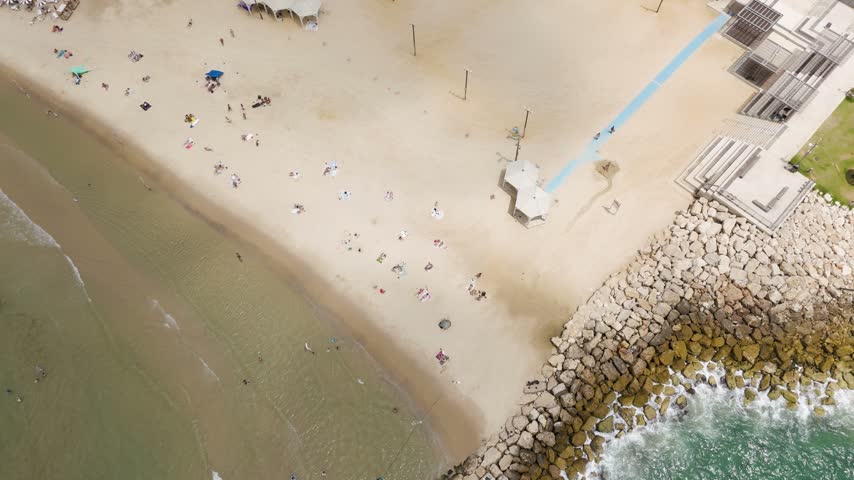 Aerial view of the sandy beach in Tel Aviv-Yafo with people relaxing on the sand, a stone breakwater, and clear water in Tel Aviv-Yafo, Tel Aviv District, Israel.
