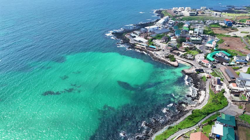 Aerial view of a coastal town with turquoise water, rocky shoreline, and buildings in Cheju, Jeju-do, South Korea.