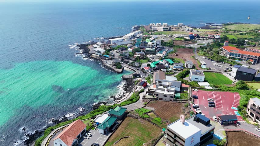 Aerial view of coastal village with turquoise waters, rocky shoreline, and modern buildings in Cheju, Jeju-do, South Korea.