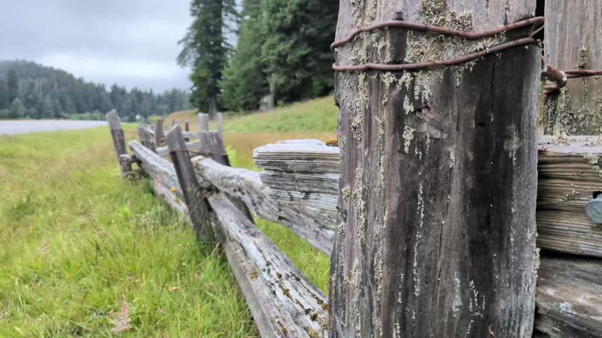Perspective view along a rustic weathered split-rail wooden fence line stretching across a grassy meadow.