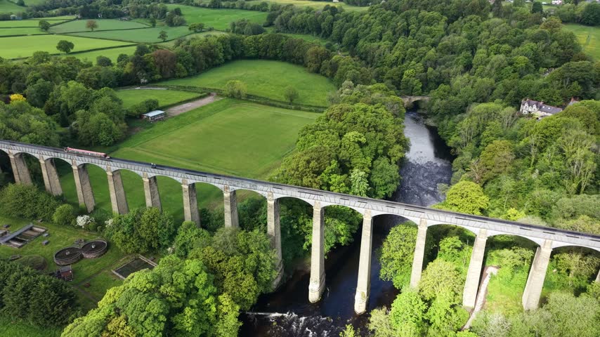 Aerial view of historic Pontcysyllte aqueduct with narrowboat crossing high above river Dee in scenic Welsh countryside.