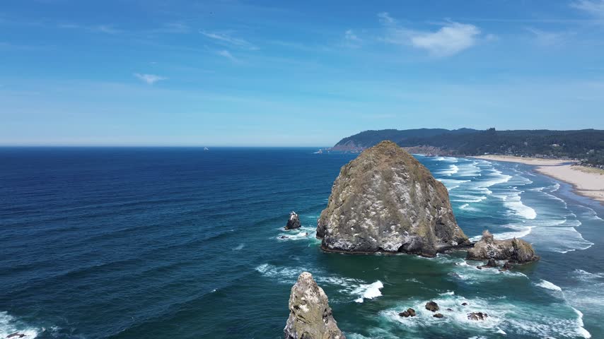 Aerial close approach to a huge coastal rock with beach and seaside town of Cannon Beach Oregon behind