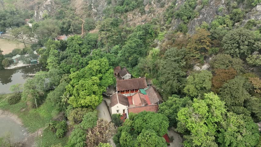 Rising aerial reveal from a small temple among trees to the limestone karst hill, ponds and rice fields around Chùa Trầm, Hanoi, Vietnam.