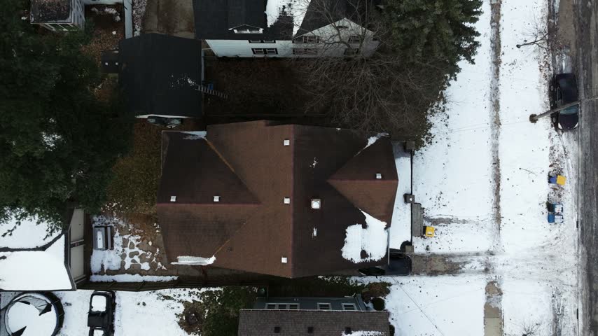Aerial view of a residential house with a brown roof surrounded by snow-covered yards and trees in a neighborhood in Grand Rapids, Michigan, United States.