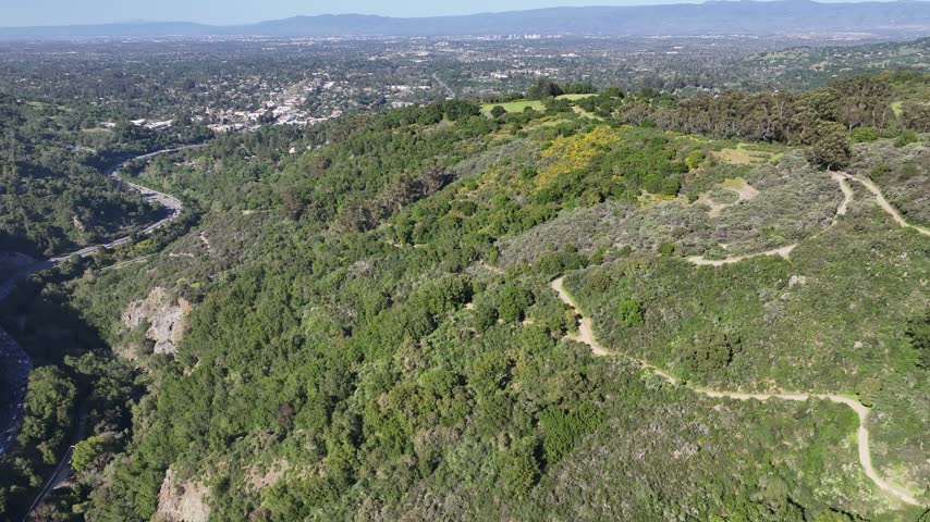 Aerial drone footage of spring-green hills and hiking trails above Silicon Valley in the Santa Cruz Mountain foothills, California, USA. A slow flight along grassy ridgelines with the valley spread out below, ideal for outdoor recreation promos, trail and fitness content, Bay Area travel, real estate reels and fresh seasonal backgrounds. 4K UHD, no audio, REC 709, no people.