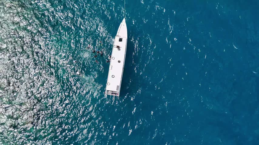Aerial view of a white boat with people swimming in the deep blue sea of Karimunjawa, Central Java, Indonesia.