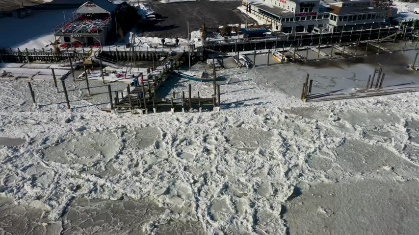 Aerial view of frozen harbor with ice floes and wooden piers near waterfront buildings in Highlands, New Jersey, United States.