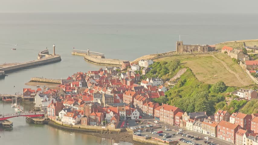 Whitby Harbour with River Esk, West Pier, East Pier, harbour lighthouses, Whitby Abbey and St Marys Church beside North Sea in North Yorkshire, England, United Kingdom, drone ascent