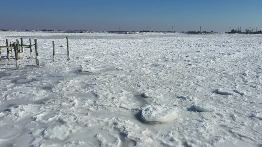 Aerial view of a frozen bay with wooden pilings and ice floes under a clear blue sky in Highlands, New Jersey, United States.