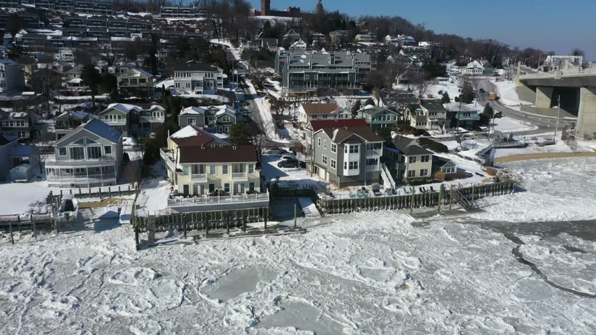 Aerial view of snowy residential houses along the frozen, ice-covered coastline in Highlands, New Jersey, United States.