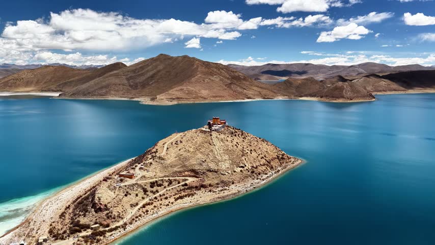 A serene Buddhist temple sits atop a rugged peninsula overlooking the crystal clear turquoise waters of a high-altitude lake.