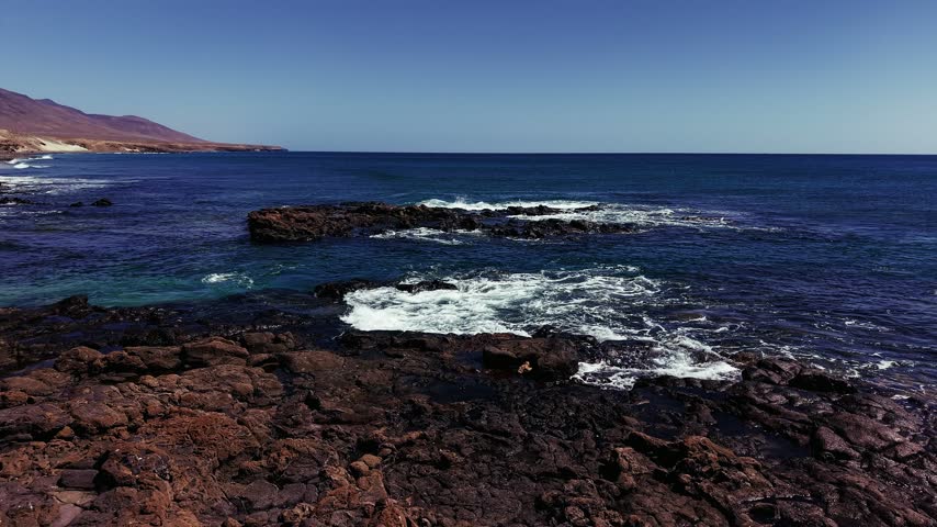 Waves crashing against the rough volcanic rock shore at Cueva Negra de Caleta along the rugged coastline in Fuerteventura