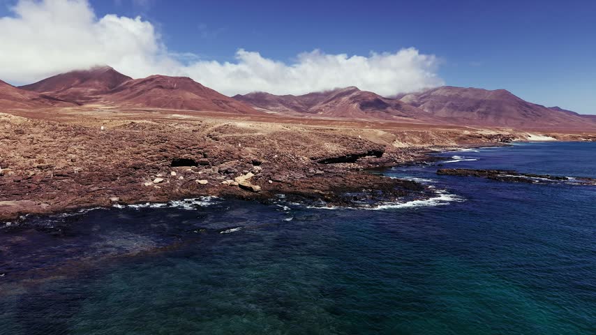 drone orbit around Waves crashing against the rough volcanic rock shore at Cueva Negra de Caleta in Fuerteventura