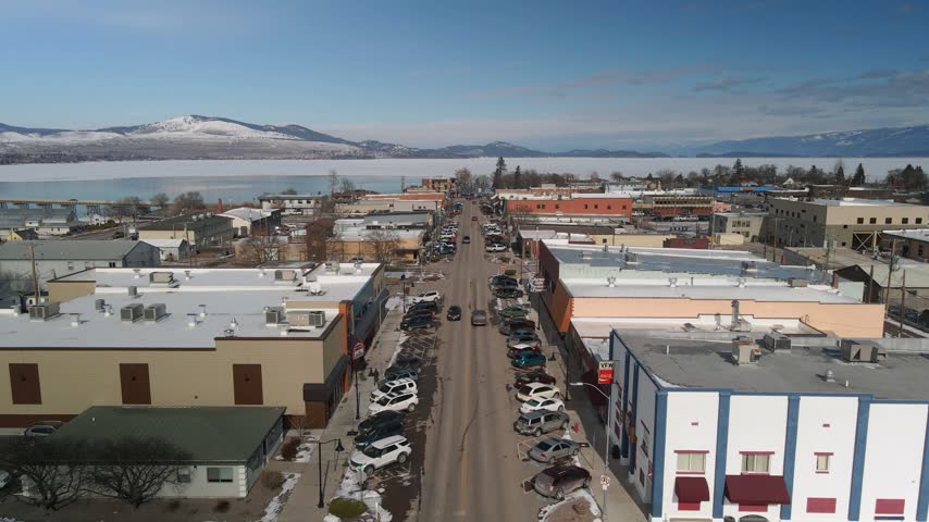 4K aerial drone view over Main Street in Polson, Montana, looking toward Flathead Lake with mountains in the background.