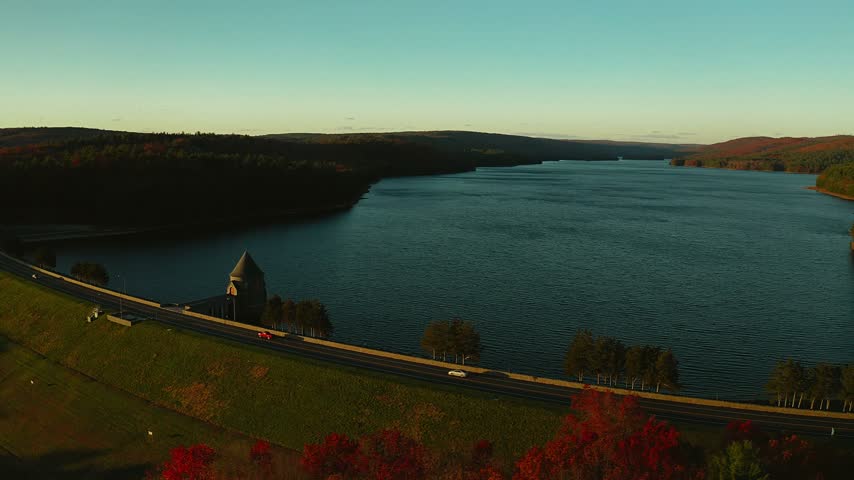 The highway dam at Barkhamsted Reservoir in Connecticut framed by fall foliage at a golden sunset