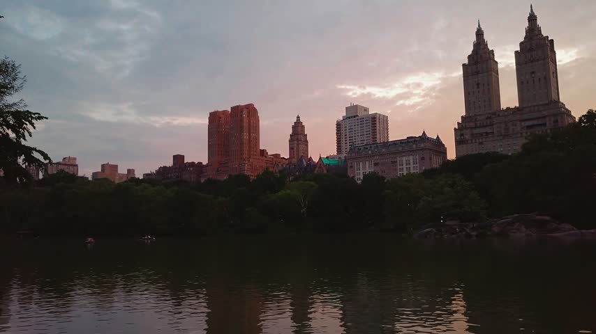 Looking out over the serene Central Park lake in New York with the iconic city skyline at golden sunset