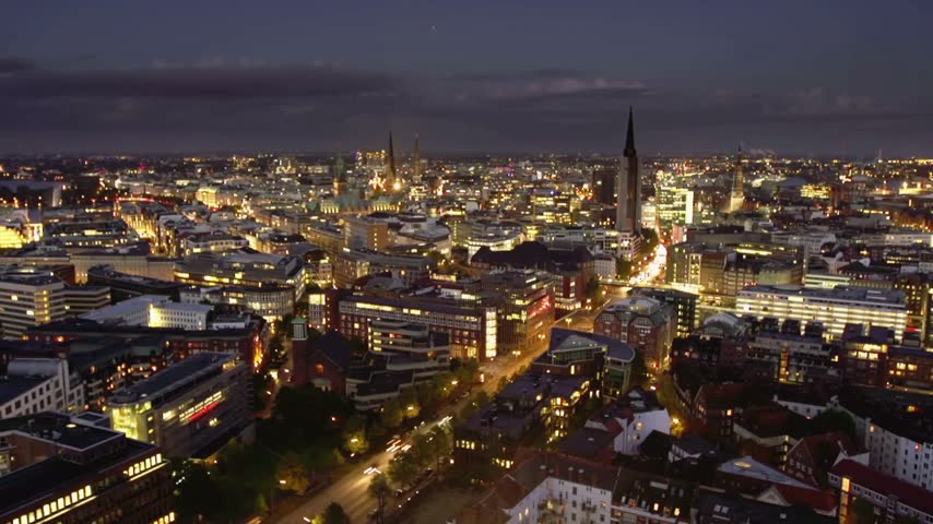 4K aerial drone view of Hamburg, Germany at night, showcasing the illuminated city skyline, urban architecture, waterfront, and glowing city lights after dark.