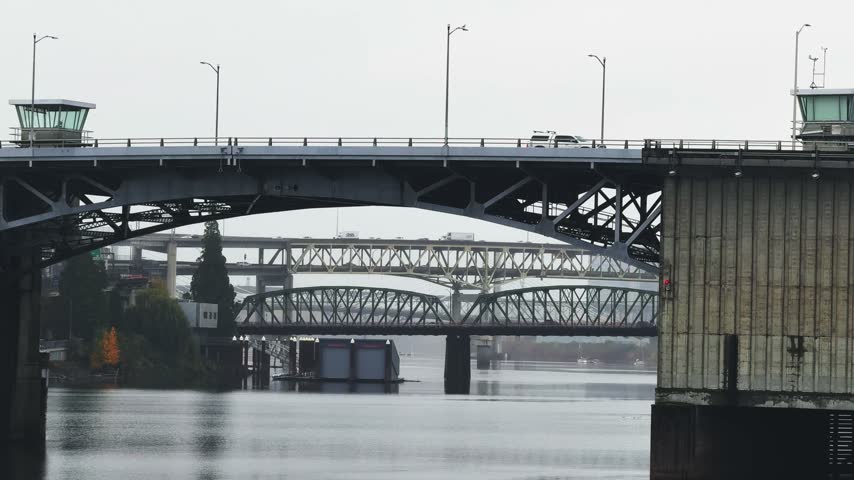 Handheld landscape shot of the SE Morrison and Hawthorne bridges spanning the Willamette River from the Waterfront in busy downtown Portland, Oregon, on a cold, gray, overcast November day in autumn.