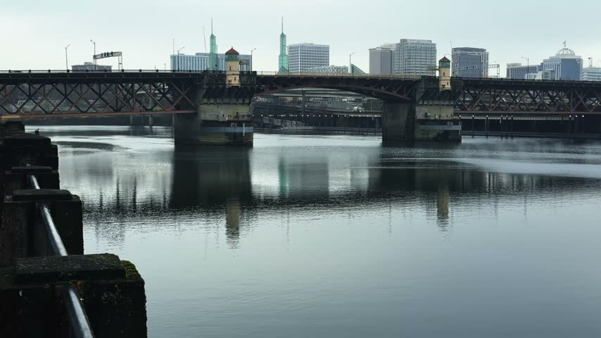 Tilt-up handheld landscape shot of the famous double-deck Steel Bridge spanning the Willamette River from the Waterfront in downtown Portland, Oregon, on a cold, overcast November day in autumn.
