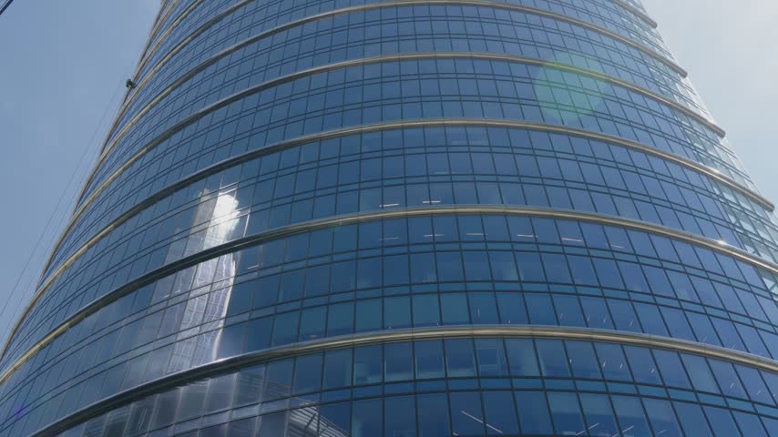 Low angle view of a modern office building with a curved glass facade. Sun reflecting on the blue windows of the financial district skyscraper
