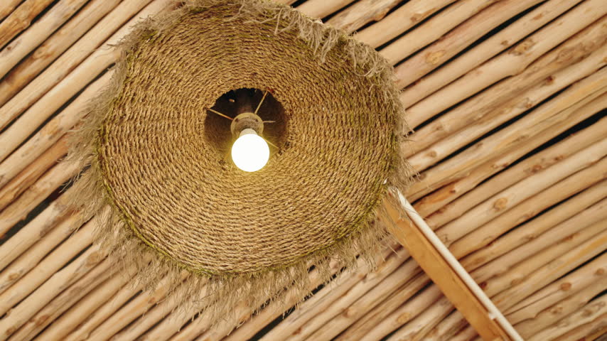 A woven pendant lamp sways gently beneath a bamboo ceiling, creating a warm tropical interior detail.