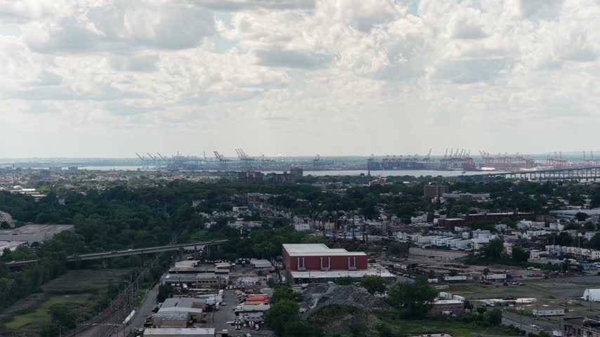 Aerial view of a tree lined urban waterfront with docks, boats and buildings beneath a cloudy sky.