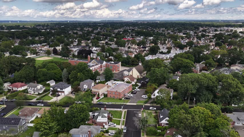 A broad drone view shows detached houses and leafy blocks with larger brick buildings scattered through the neighborhood.