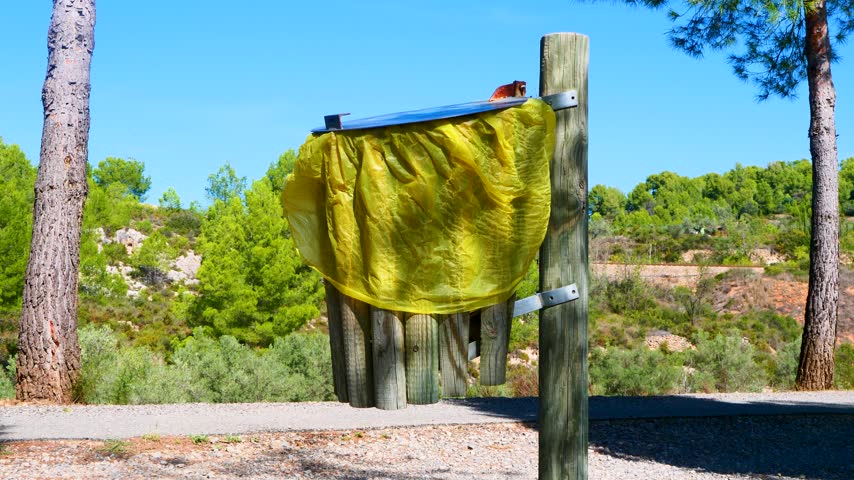 Wooden park trash bin with large yellow garbage bag standing by nature trail. Ideal for ecological awareness campaign website, city municipal service presentation or plastic waste management promo