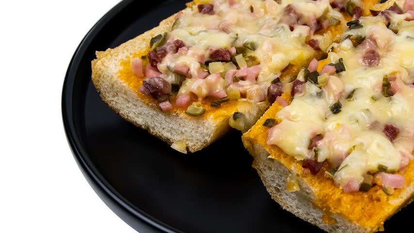 Toasted bread slices topped with melted cheese, diced ham, chopped vegetables, and herbs, served on a black plate.