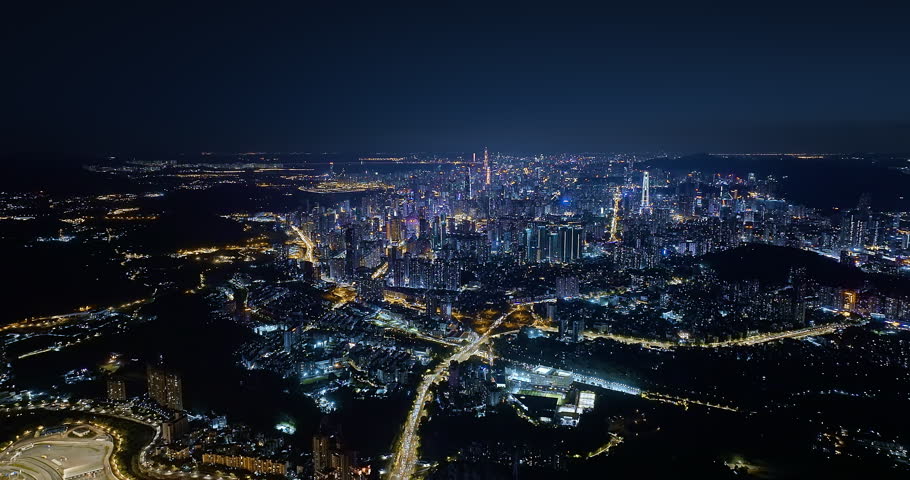 High angle panoramic view of Shenzhen city skyline illuminated at night, showing modern skyscrapers and glowing roads.