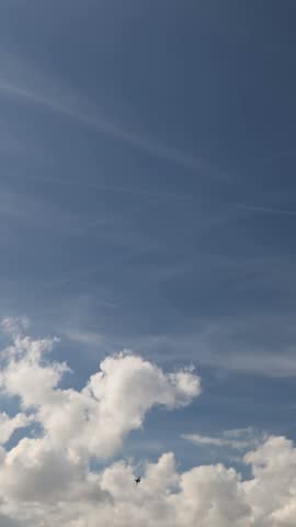Vertical screen Fighter jet flies beneath towering white clouds across a vast blue sky leaving a faint trail during an aerial display with dramatic summer weather above