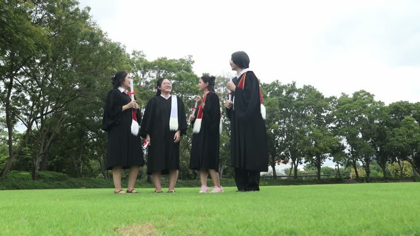 Group male and female university students dressed in graduation gowns and holding their bachelor’s degree diplomas jump high in the air with joy on the campus lawn celebrating their academic achievement.