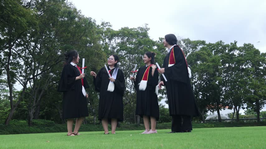 Group male and female university students dressed in graduation gowns and holding their bachelor’s degree diplomas jump high in the air with joy on the campus lawn celebrating their academic achievement.
