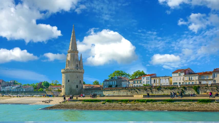 Seaside of La Rochelle dominated by Tour de la Lanterne, FranceLA   Lantern tower is one of three medieval towers in La Rochelle which guarded port; is former historic lighthouse which also served as a prison.  Lantern Tower on a sunny day in FranceLA  Lantern tower (Tour de la Lanterne) is one of three medieval towers in  which guarded port; is former historic lighthouse which also served as a prison.Time Lapse of the harbor in The famous French city on the ocean. Sunny summer day, clouds are moving in the background. Crowds of tourists walk the streets