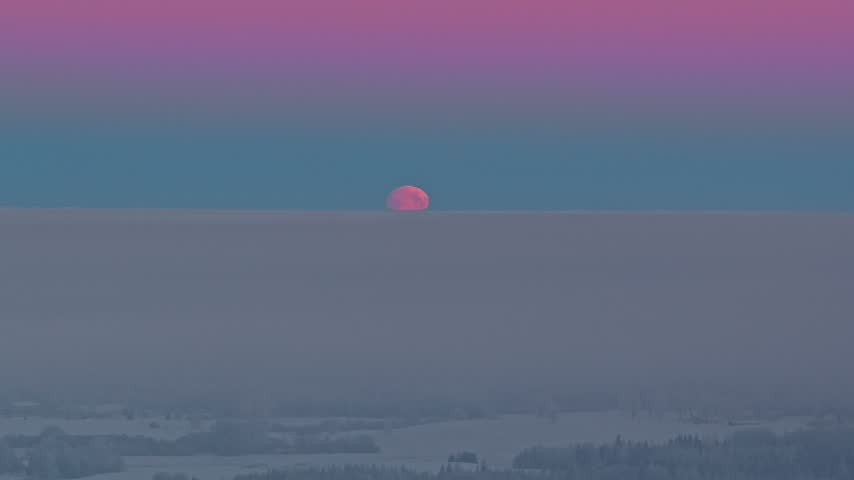 Aerial view of a red moon rising above a thick fog layer over a winter landscape in Latvia.