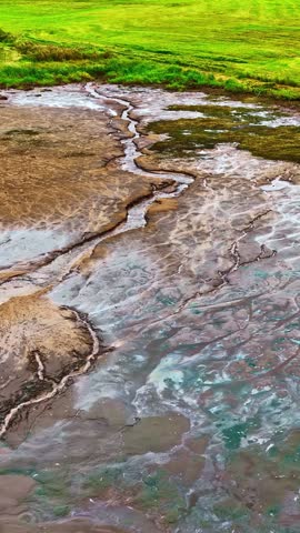 Aerial view of a winding stream cutting through textured mudflats and marshland in France.