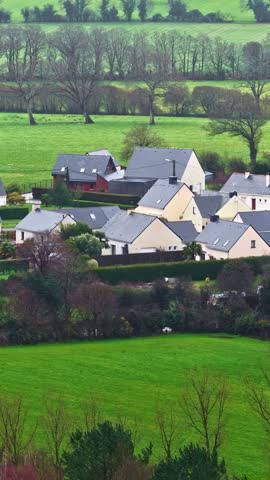 Aerial view of a small village with houses featuring slate roofs surrounded by lush green fields and hedgerows in France.
