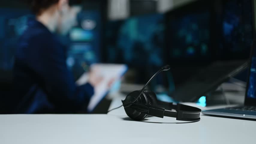 Headset on desk with professional flight controller examining radar displays and data screens in a modern command center.