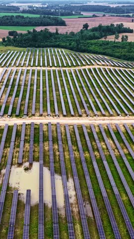 Aerial view of rows of solar panels installed in a field with patches of water and green grass in Ventspils, Latvia.